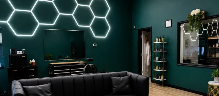 Emerald Edge lounge with a black leather sofa, glowing hexagon lights and professional hair products displayed on a gold shelf.
